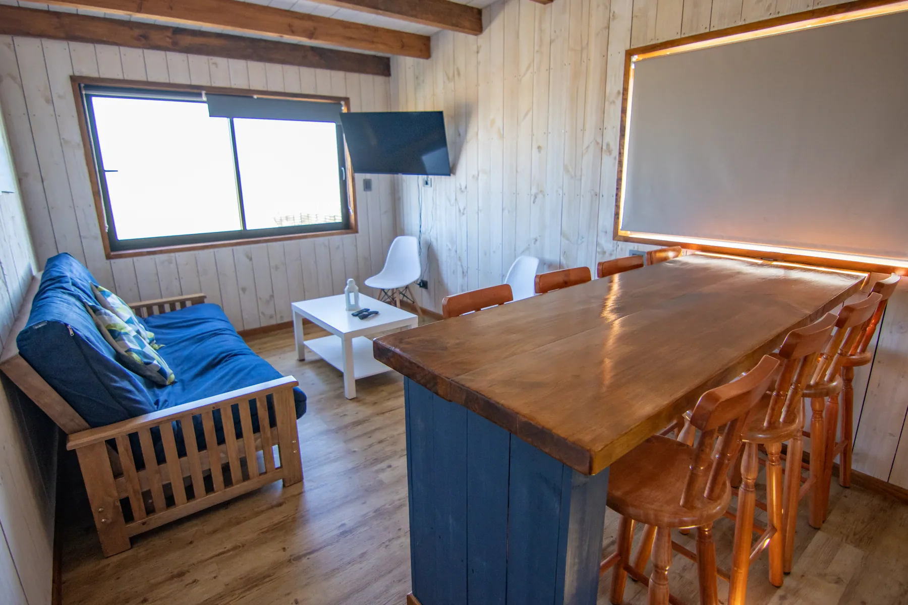 Living de la cabaña Biología con sofá cama, TV y mesa alta con banquetas de madera