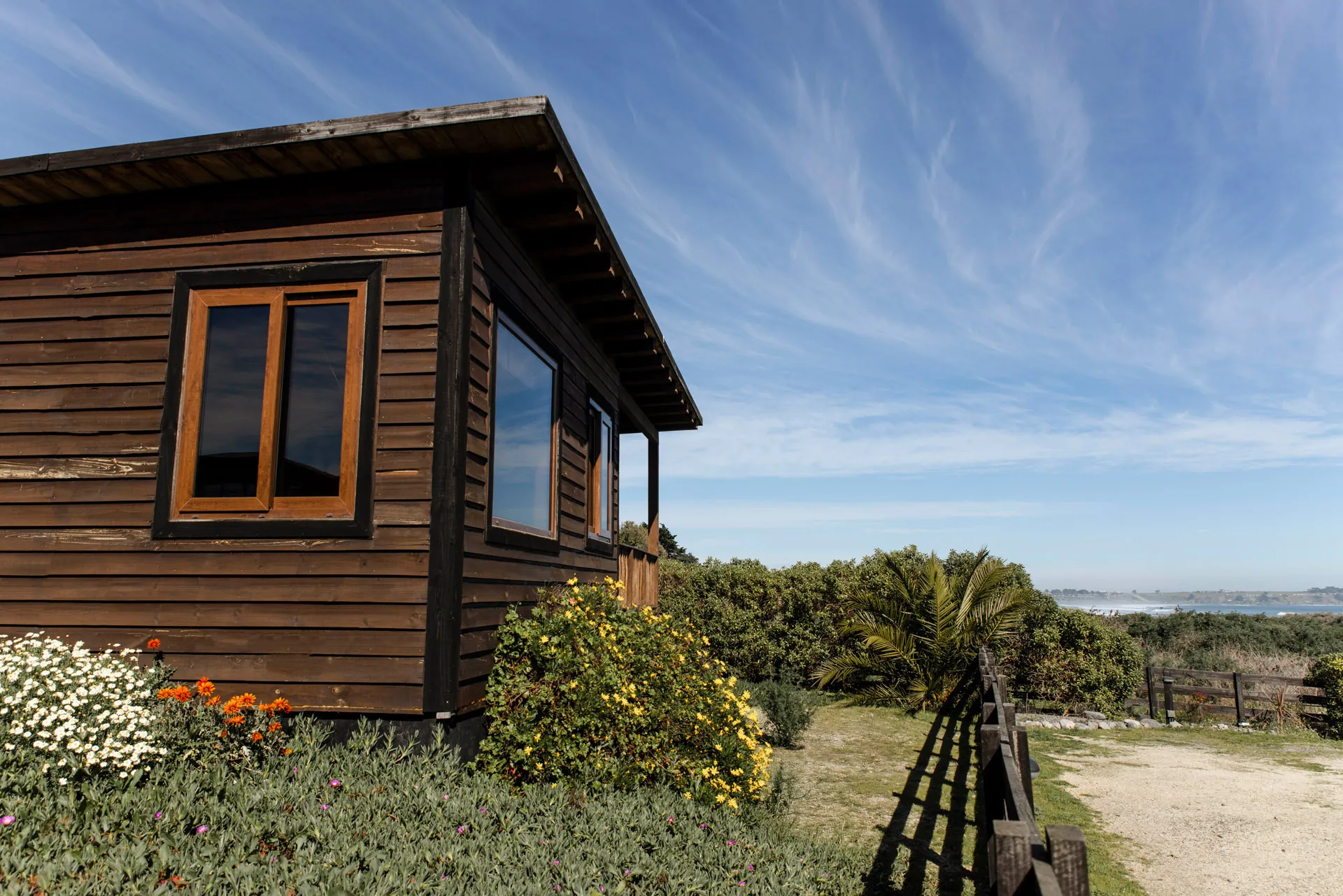 Cabaña de madera entre los jardines, con la playa de fondo
