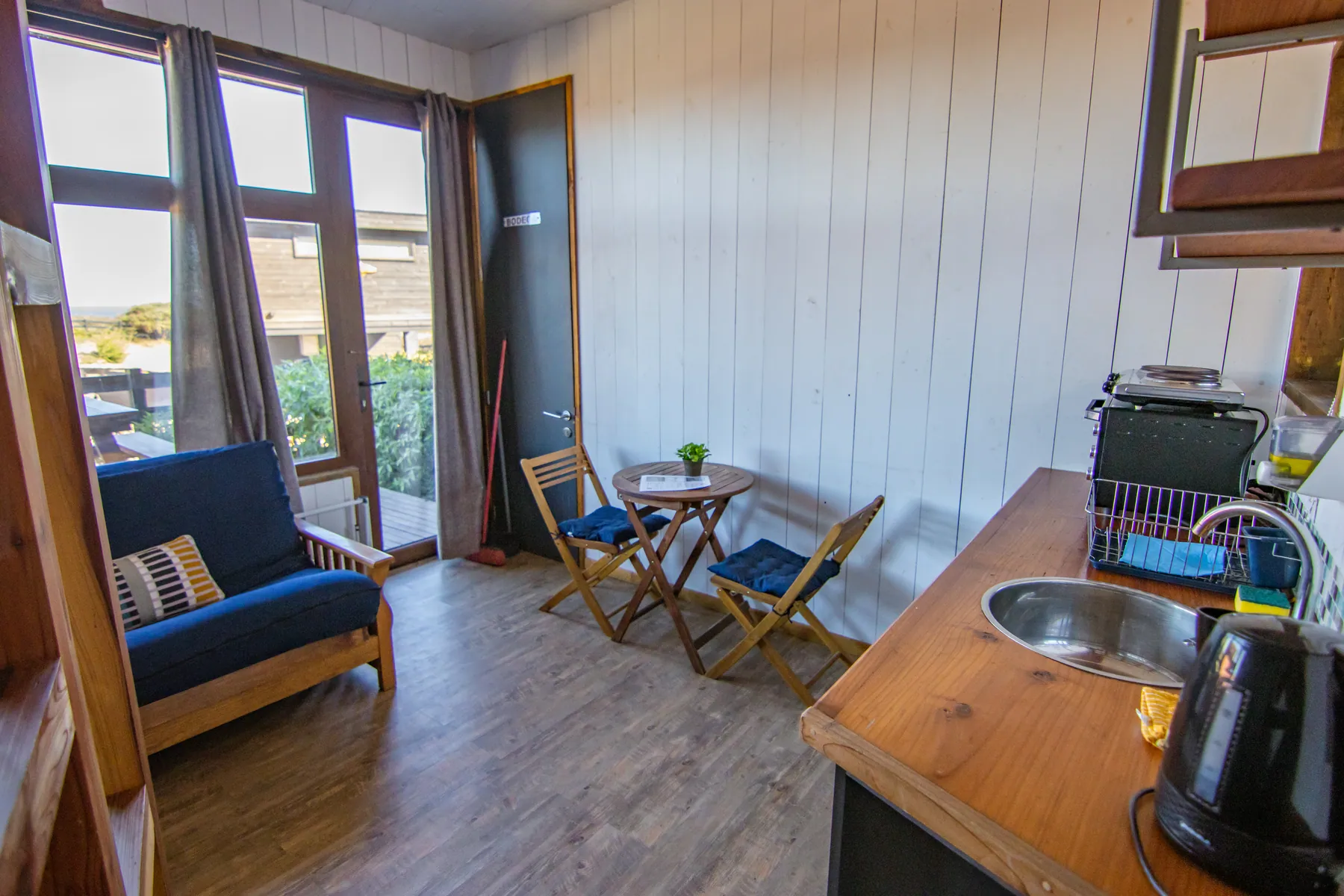 Ambiente único de la cabaña El Diamante: futón, mesa para dos y barra de cocina junto al ventanal que da a la terraza