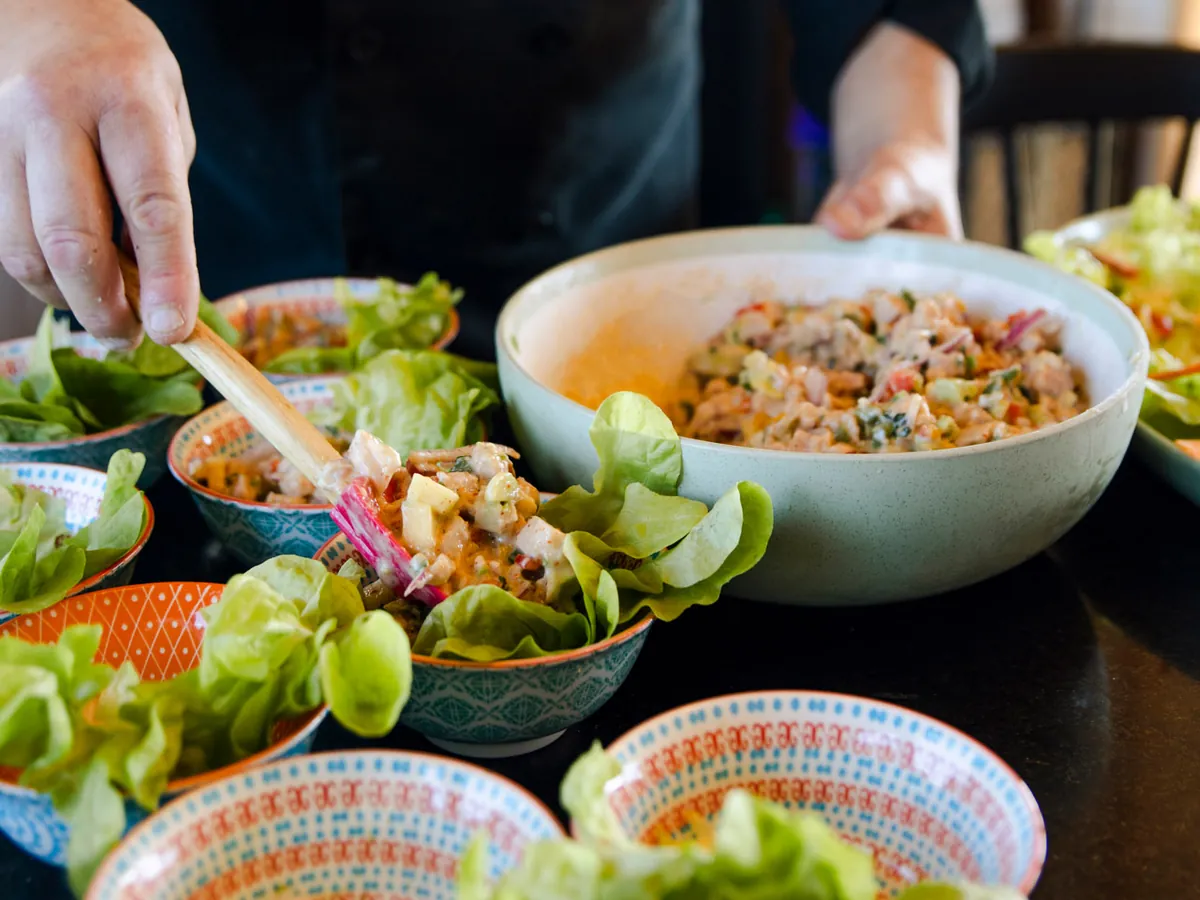 Chef sirviendo ceviche en bowls individuales sobre hojas de lechuga, para la mesa compartida de un evento en el complejo