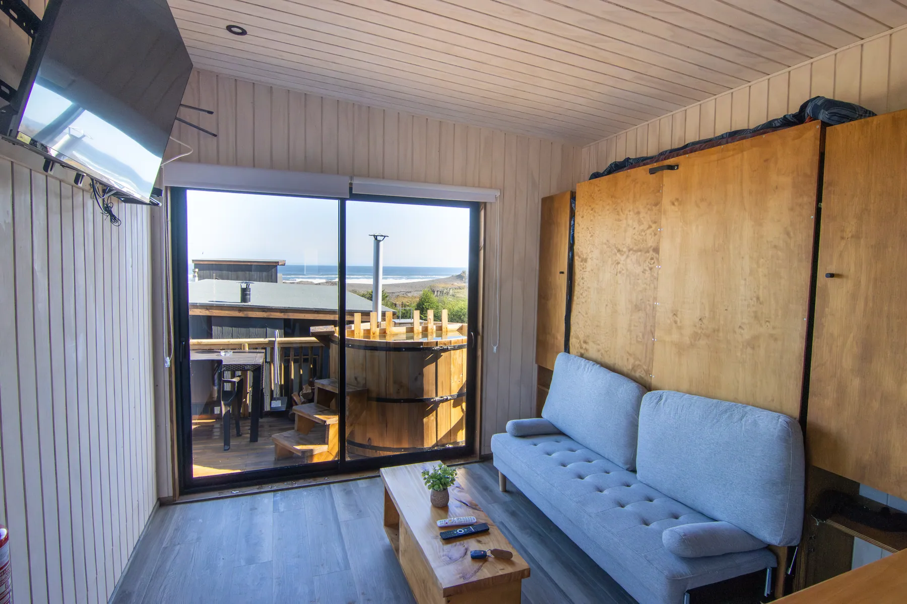 Living de la cabaña La Paloma con sofá y ventanal corredizo, con la tinaja de la terraza y el mar al fondo