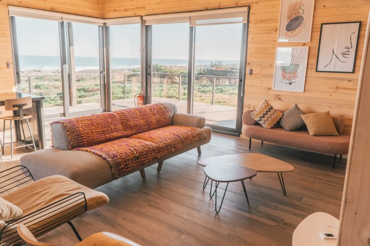 Living de la cabaña La Pancora con dos sofás y ventanales corredizos, con la playa de Punta de Lobos al frente