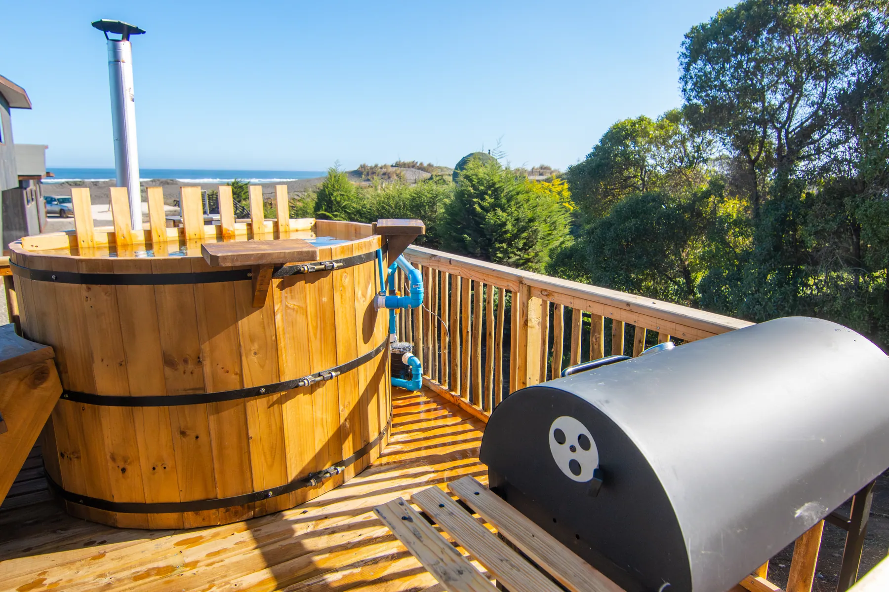 Tinaja de madera y calefactor a leña en la terraza privada de la cabaña Mar del Plata, con el mar al fondo