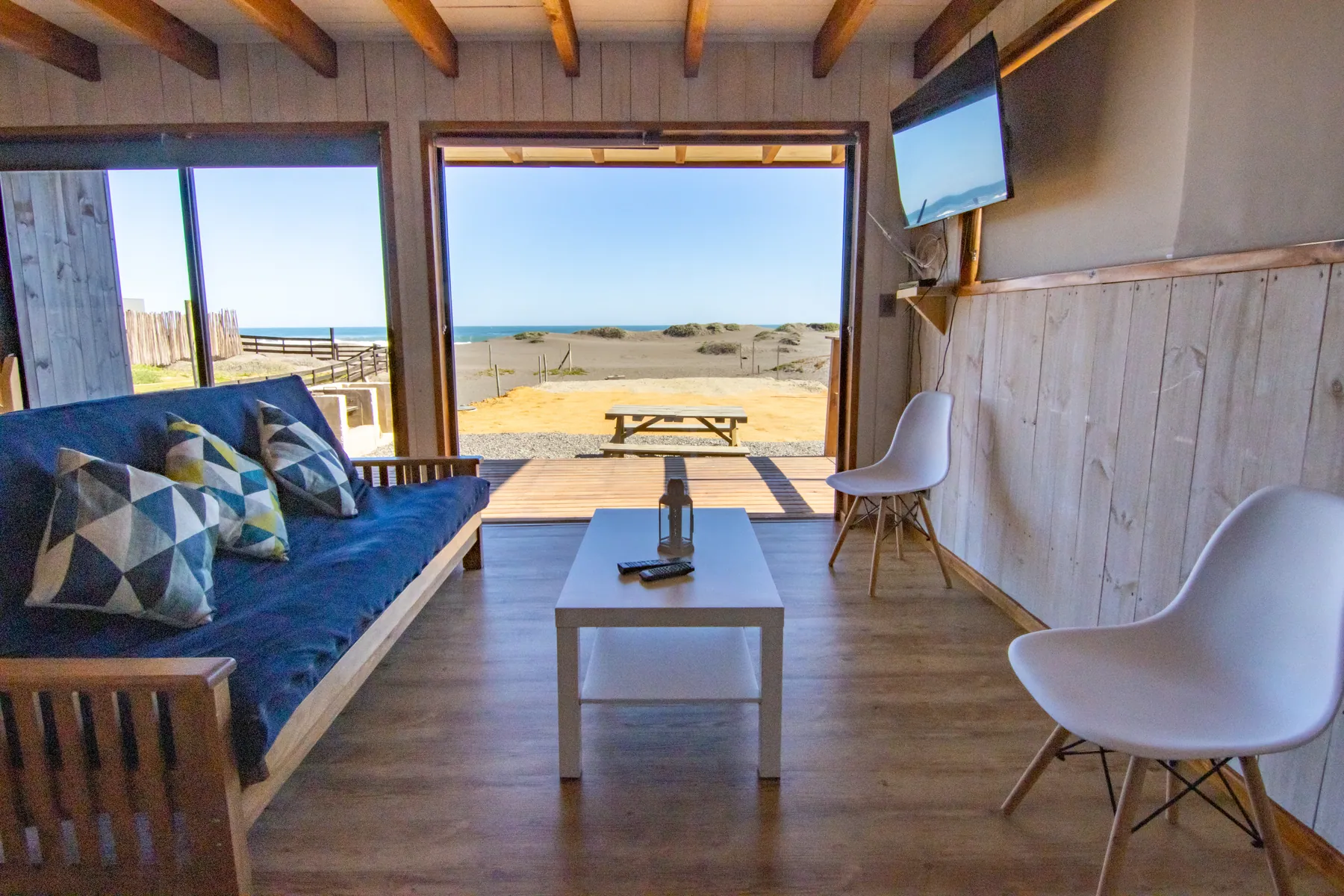 Living de la cabaña Miramar con futón y ventanal corredizo abierto a la terraza, con la playa al frente