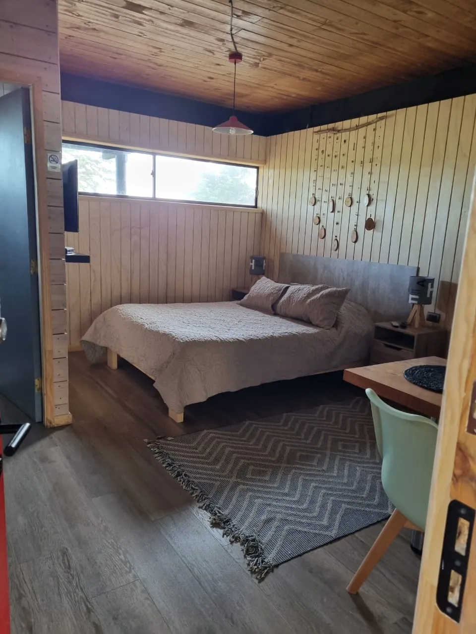 Cabaña Panilonco: ambiente único con cama de dos plazas, alfombra y rincón comedor junto a la entrada