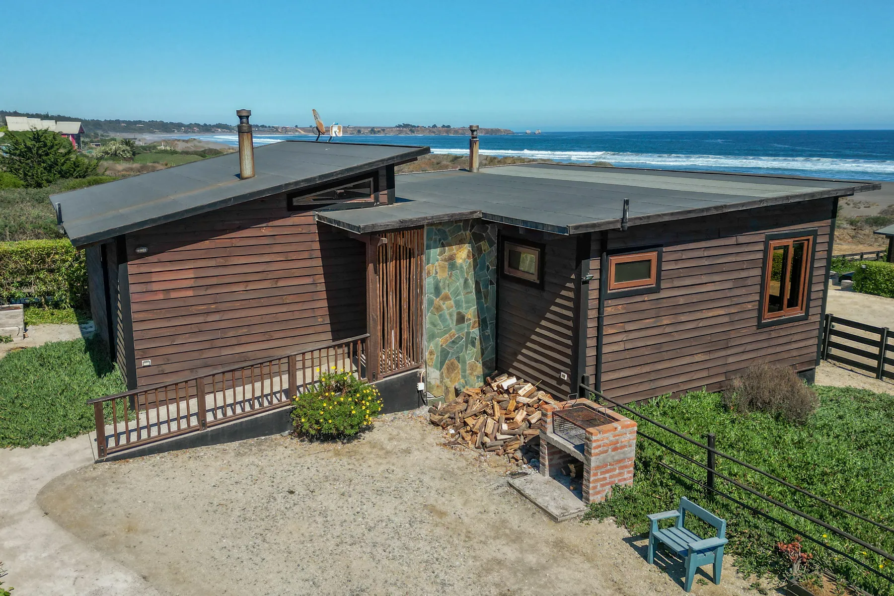 Cabaña Puertecillo vista desde afuera, de madera y piedra, con la leña apilada y la parrilla, frente al mar