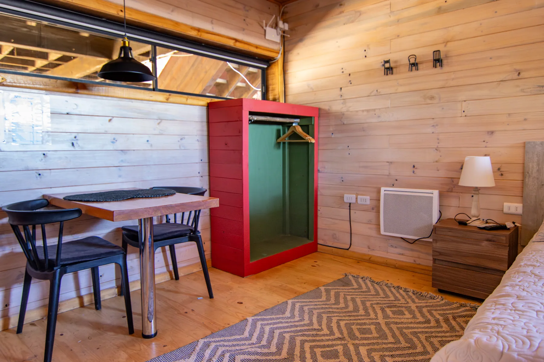 Ambiente único de la cabaña Pupuya, con mesa de comedor, ropero rojo y la cama al fondo